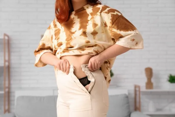 Image of woman trying to do her trousers up after pregnancy weight gain Henley In Arden